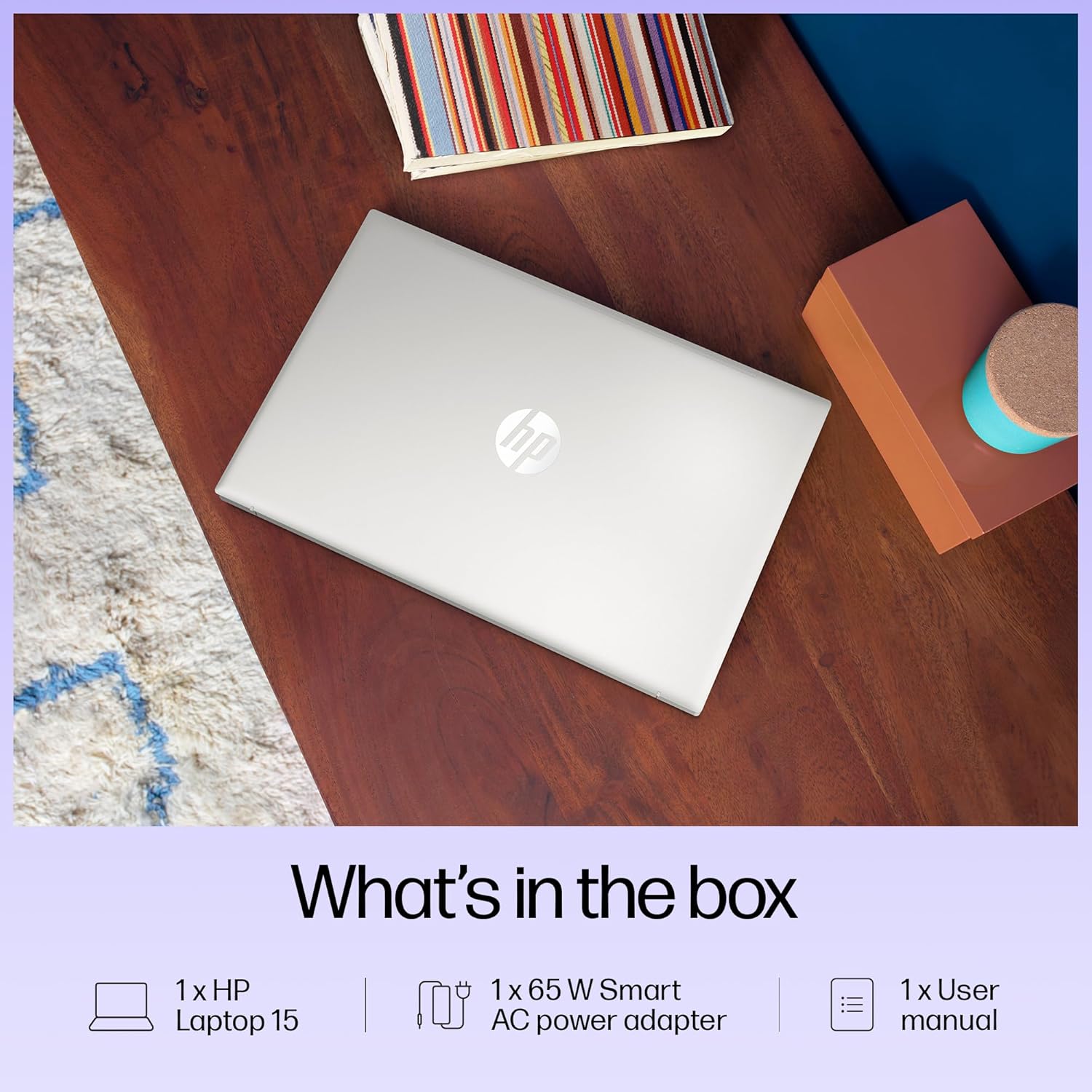 Closed silver HP 15 i3 laptop on wooden desk with power adapter and user manual