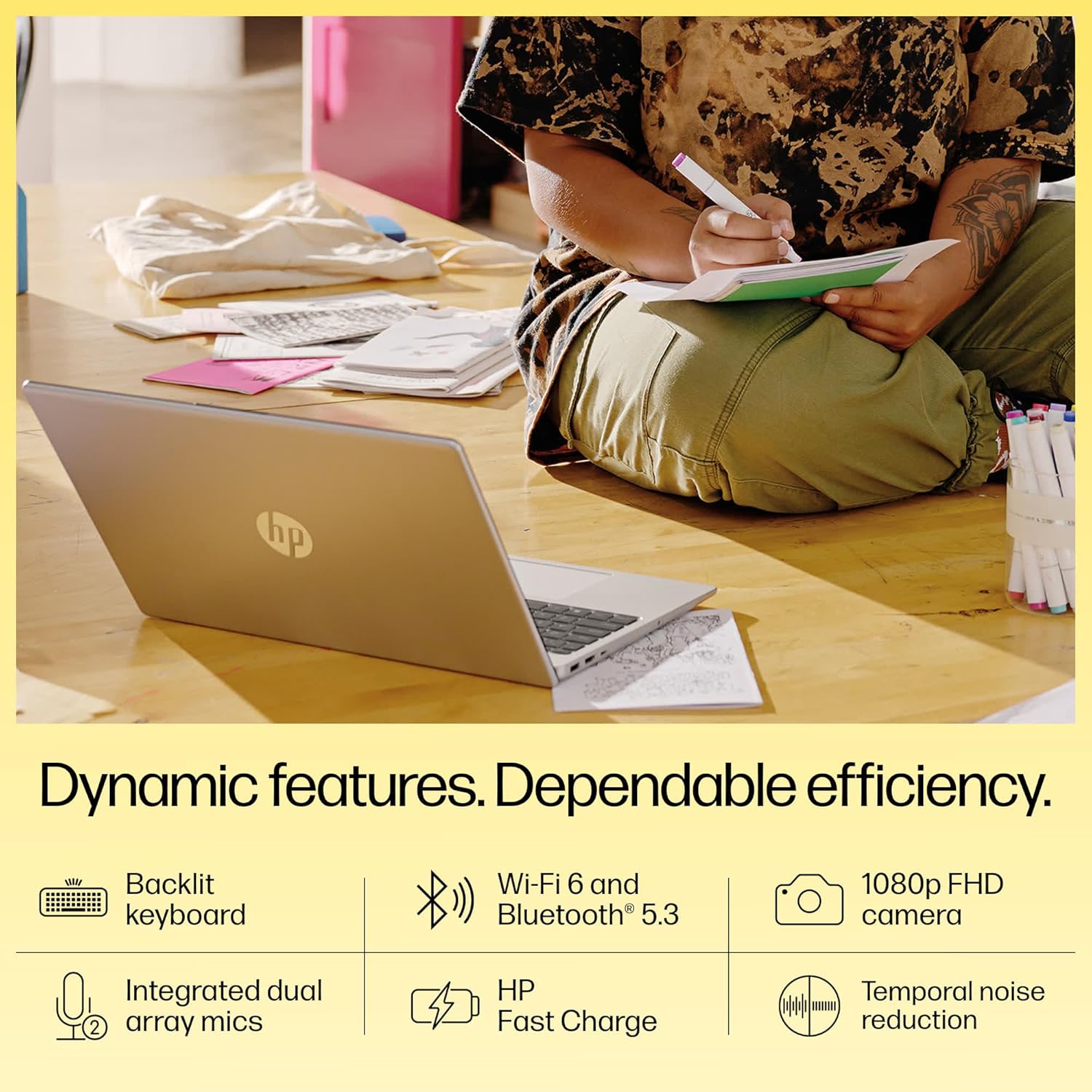 HP 15 Ryzen 5 laptop in silver on wooden table with person writing notes in the background