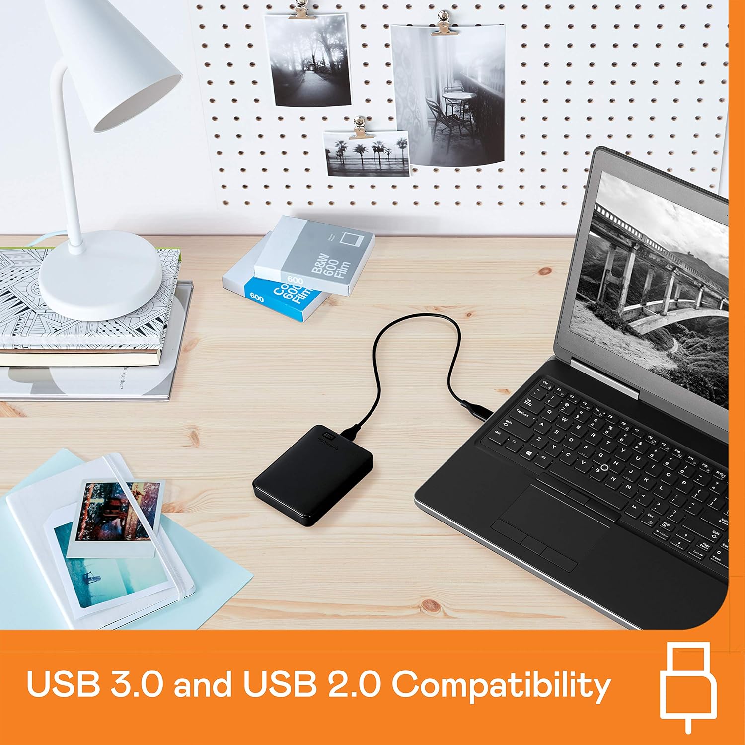 Western Digital Elements 2TB portable hard drive connected to laptop on wooden desk with lamp and photos